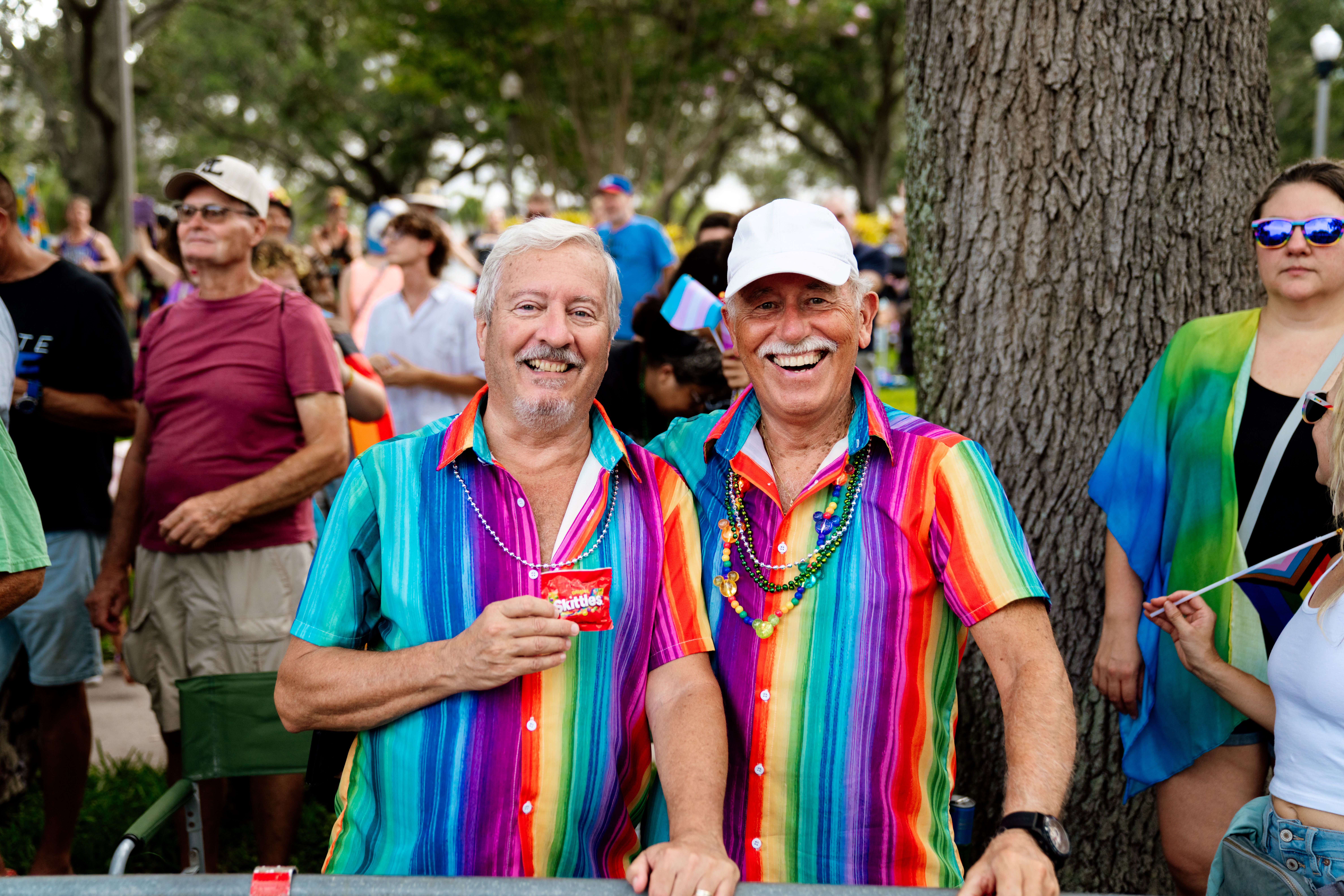 Two men smiling in a crowd with a Skittles bag