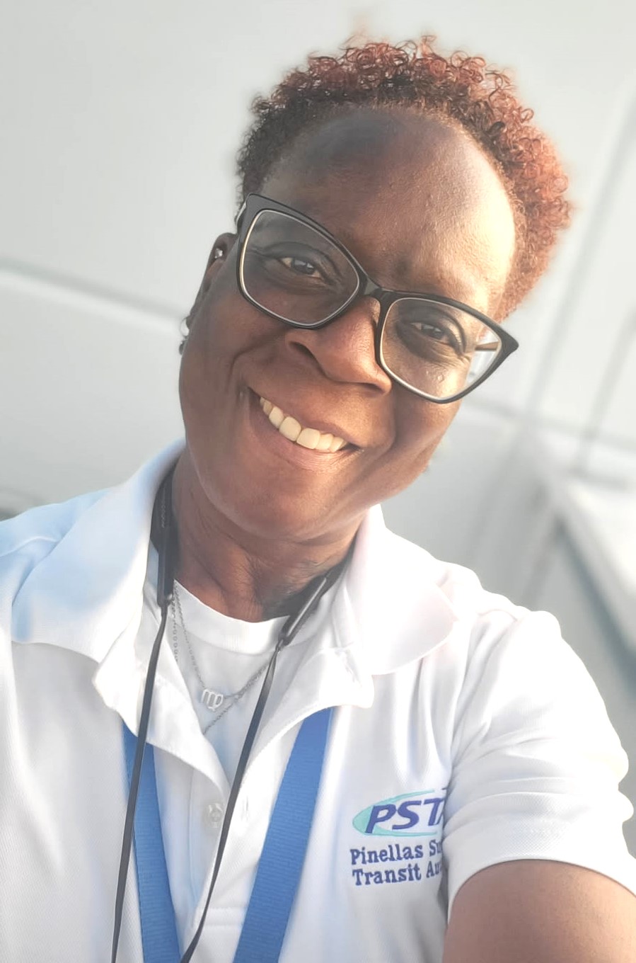 A selfie of Liz smiling and wearing a collared white PSTA shirt, black rimmed glasses, and a blue PSTA lanyard.