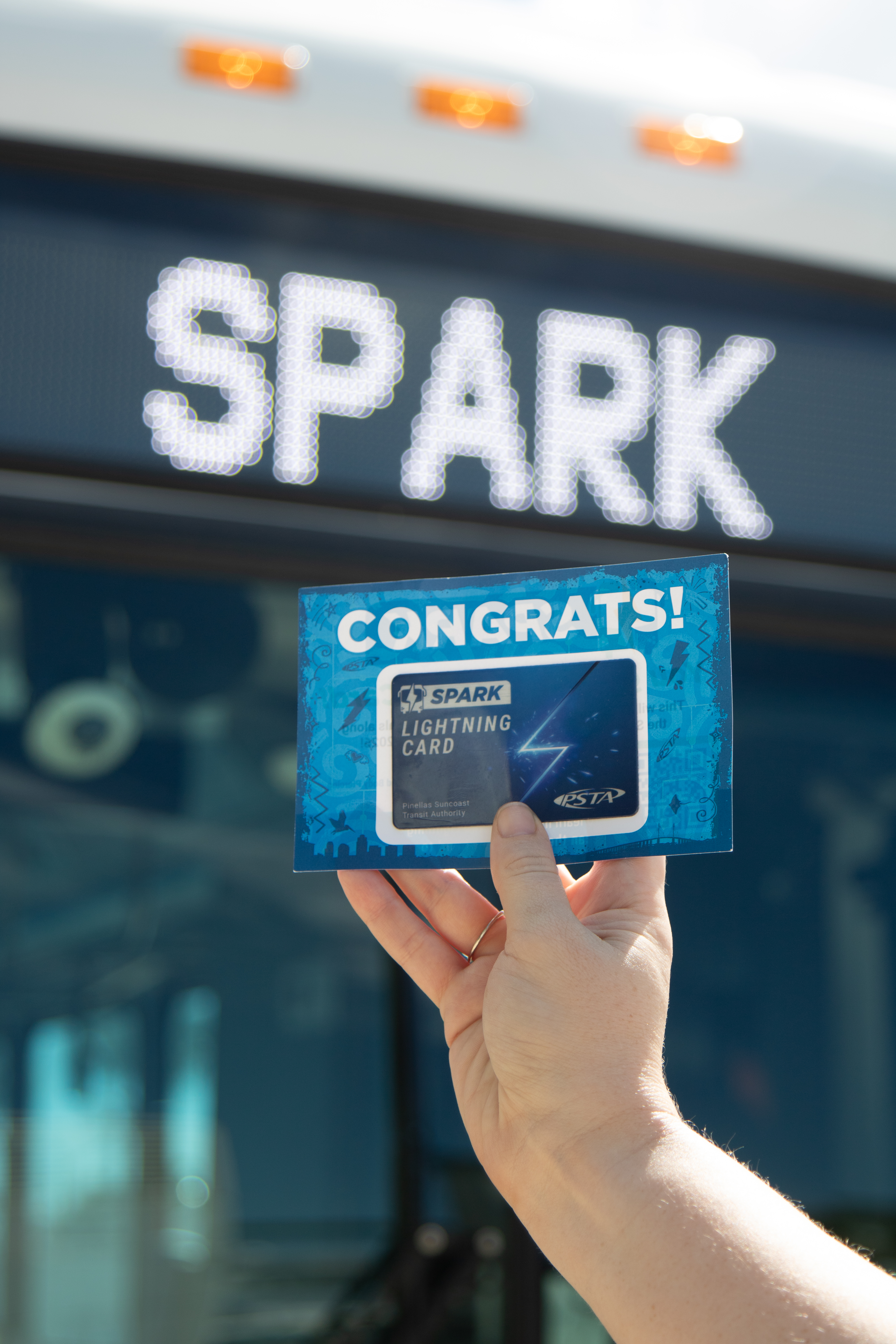 A photo of someone holding the Spark Lightning Card in front of a bus that says "Spark" on the headsign.