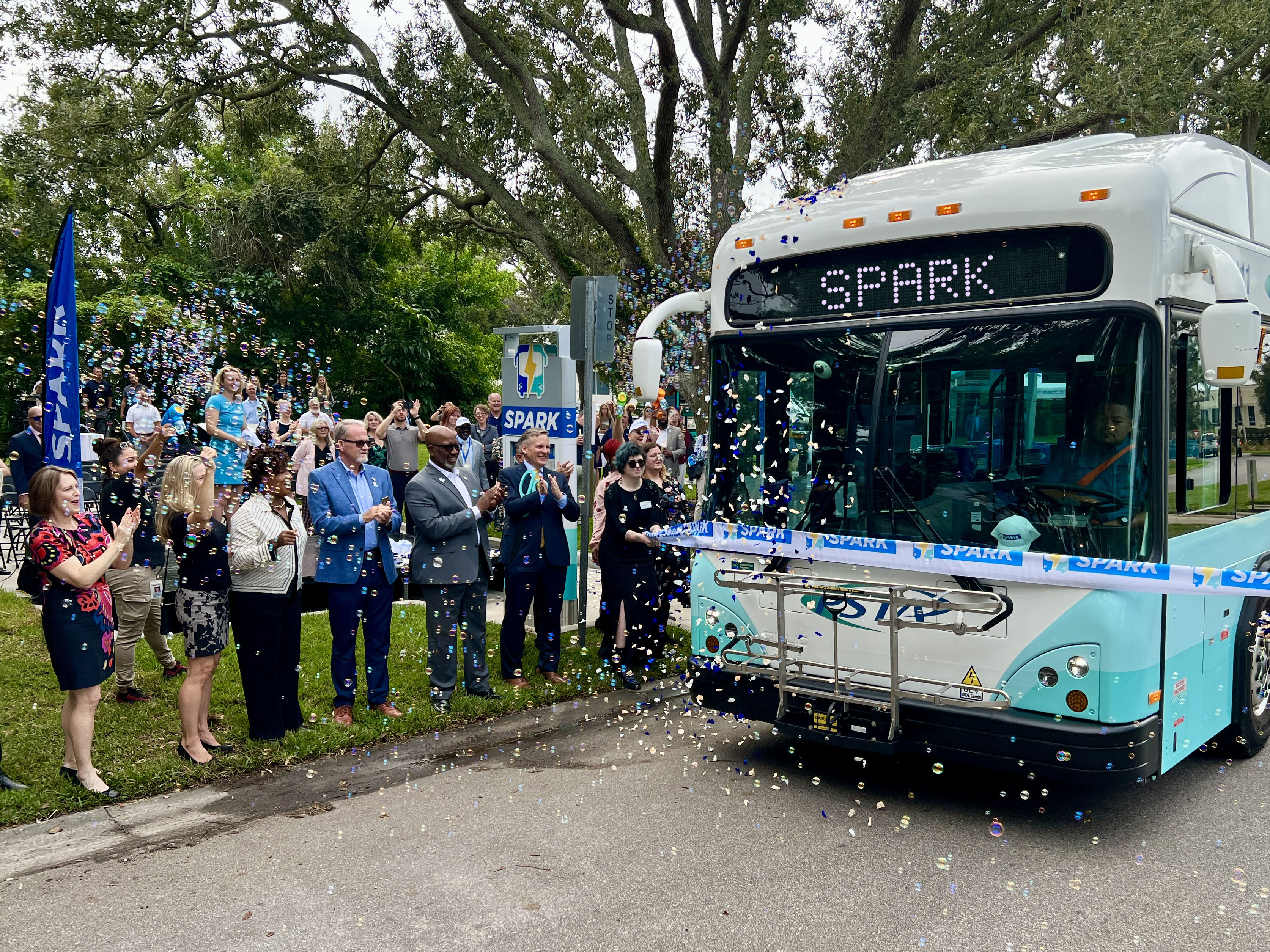 A photo of a Spark bus driving through a Spark ribbon to cut it.